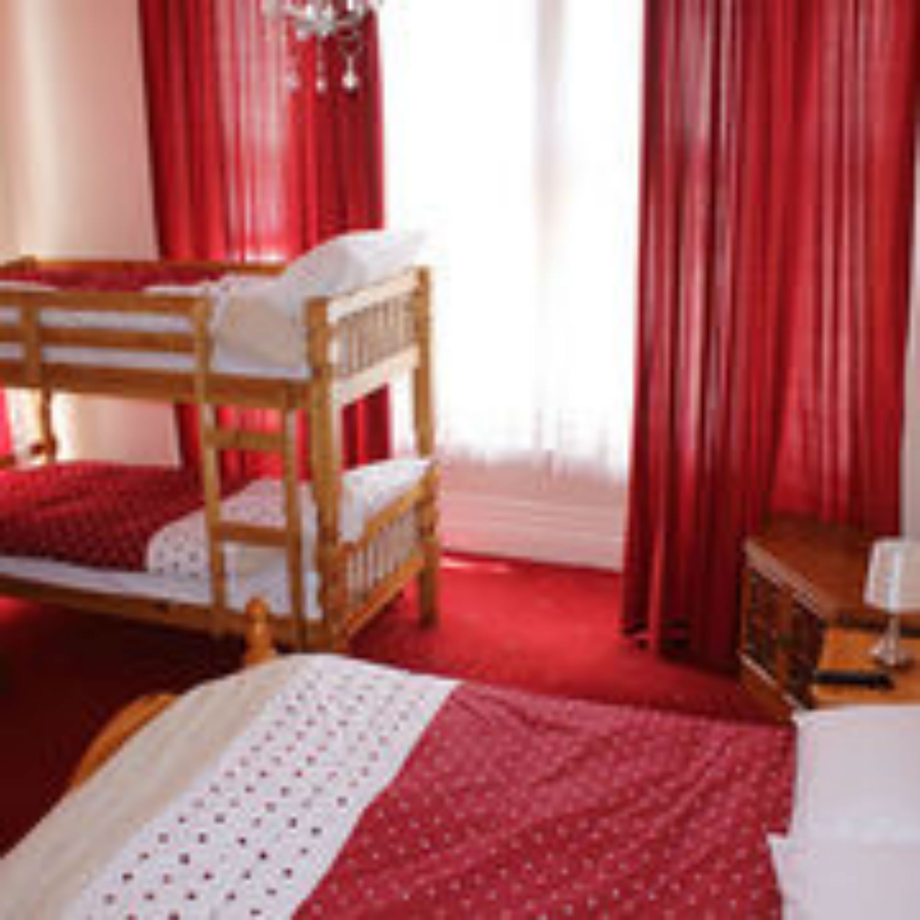 A room with a wooden bunk bed, red curtains, and a small bedside table.