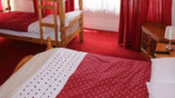 A room with a wooden bunk bed, red curtains, and a small bedside table.