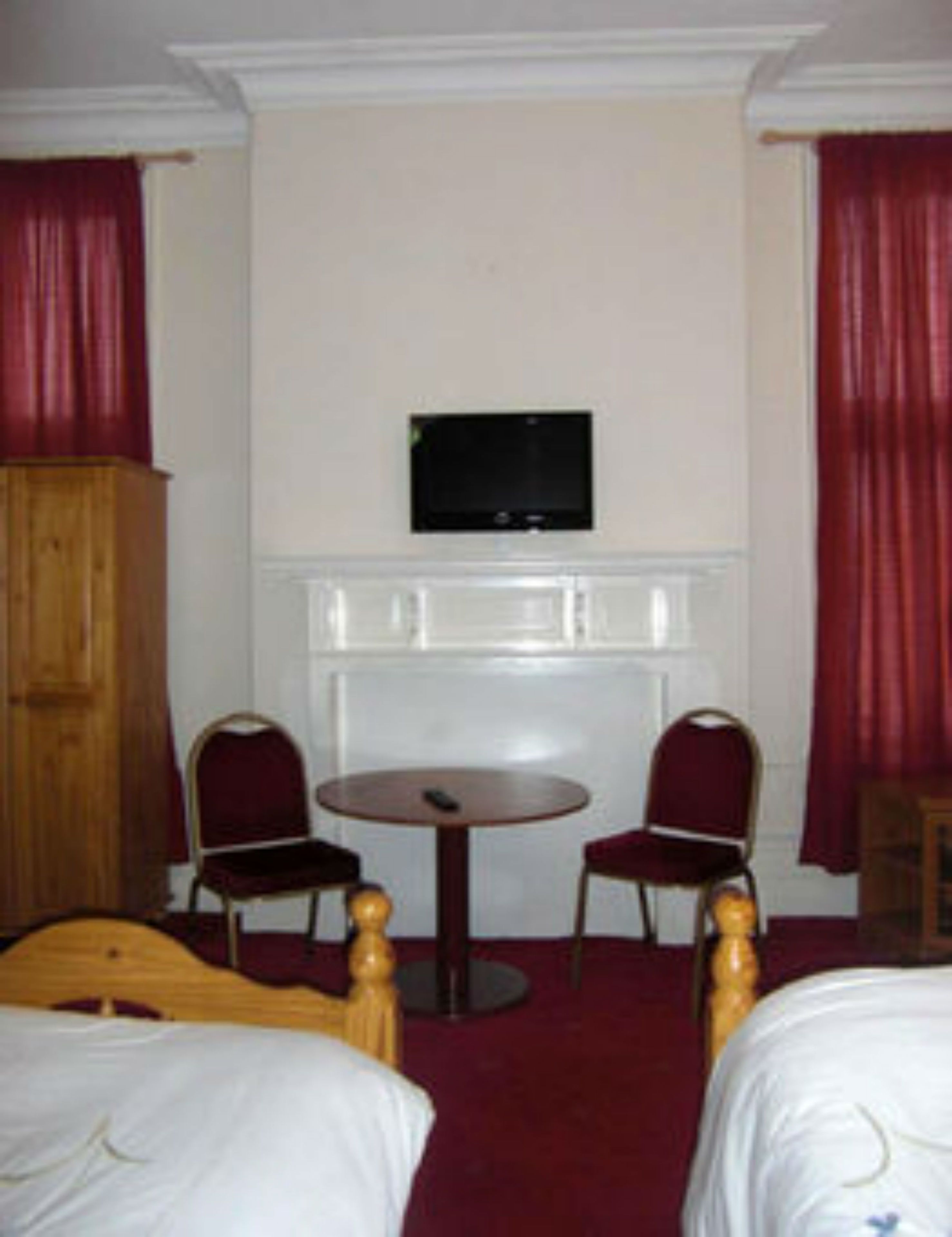 A hotel room with two beds, a round table, two chairs, a television on the wall, and a wooden wardrobe.