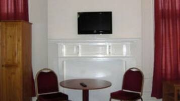 A hotel room with two beds, a round table, two chairs, a television on the wall, and a wooden wardrobe.