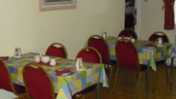 A dining area with tables covered in colorful tablecloths, red chairs, and a framed picture on the wall.