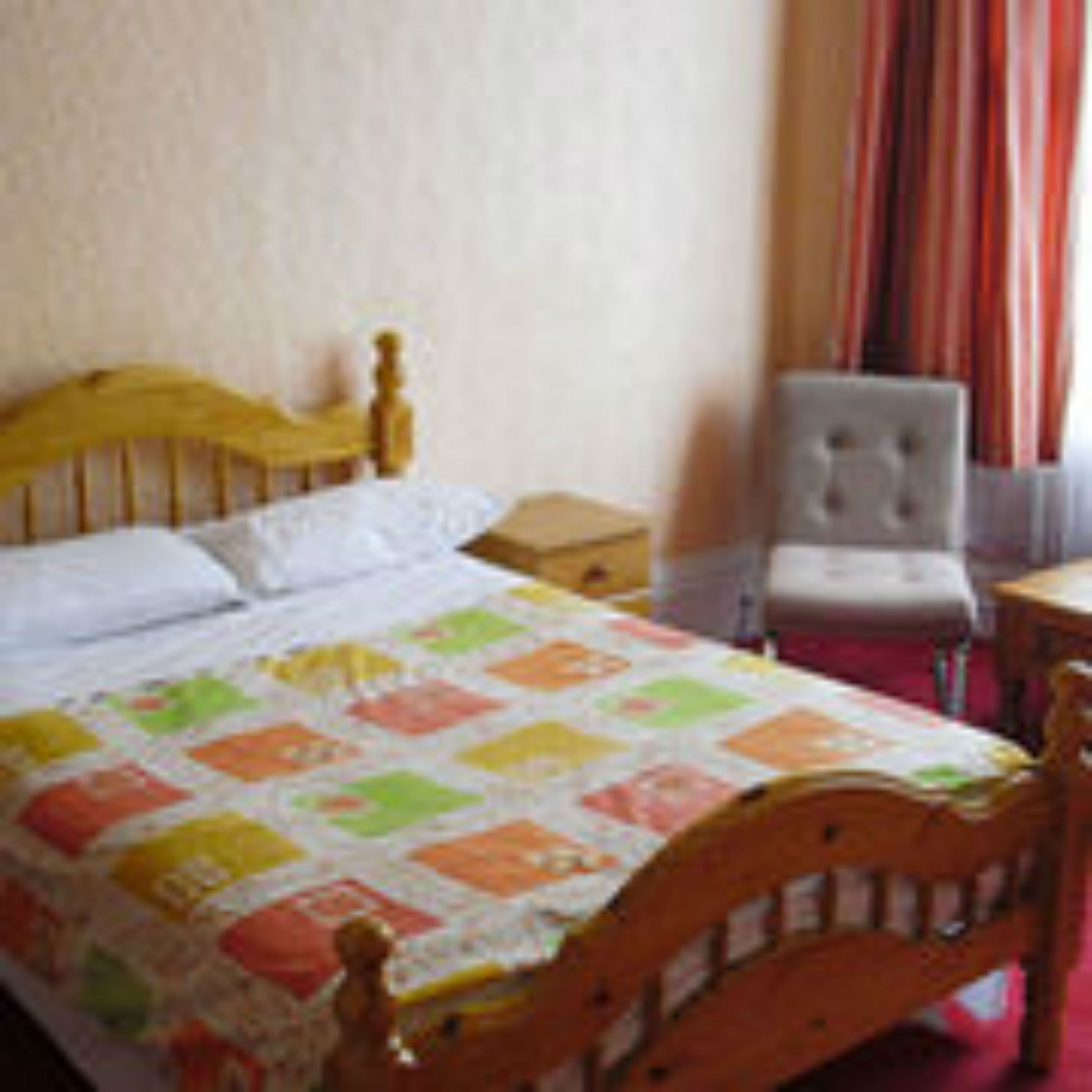 Un dormitorio con cama de madera, mesita de noche, una silla y ventana con cortinas.