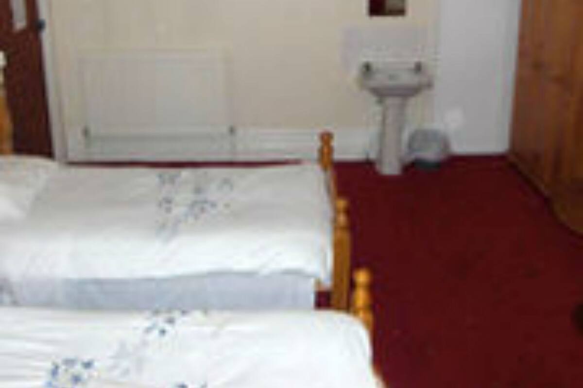 Een slaapkamer met twee eenpersoonsbedden, een radiator, een klein wastafeltje en een deur.