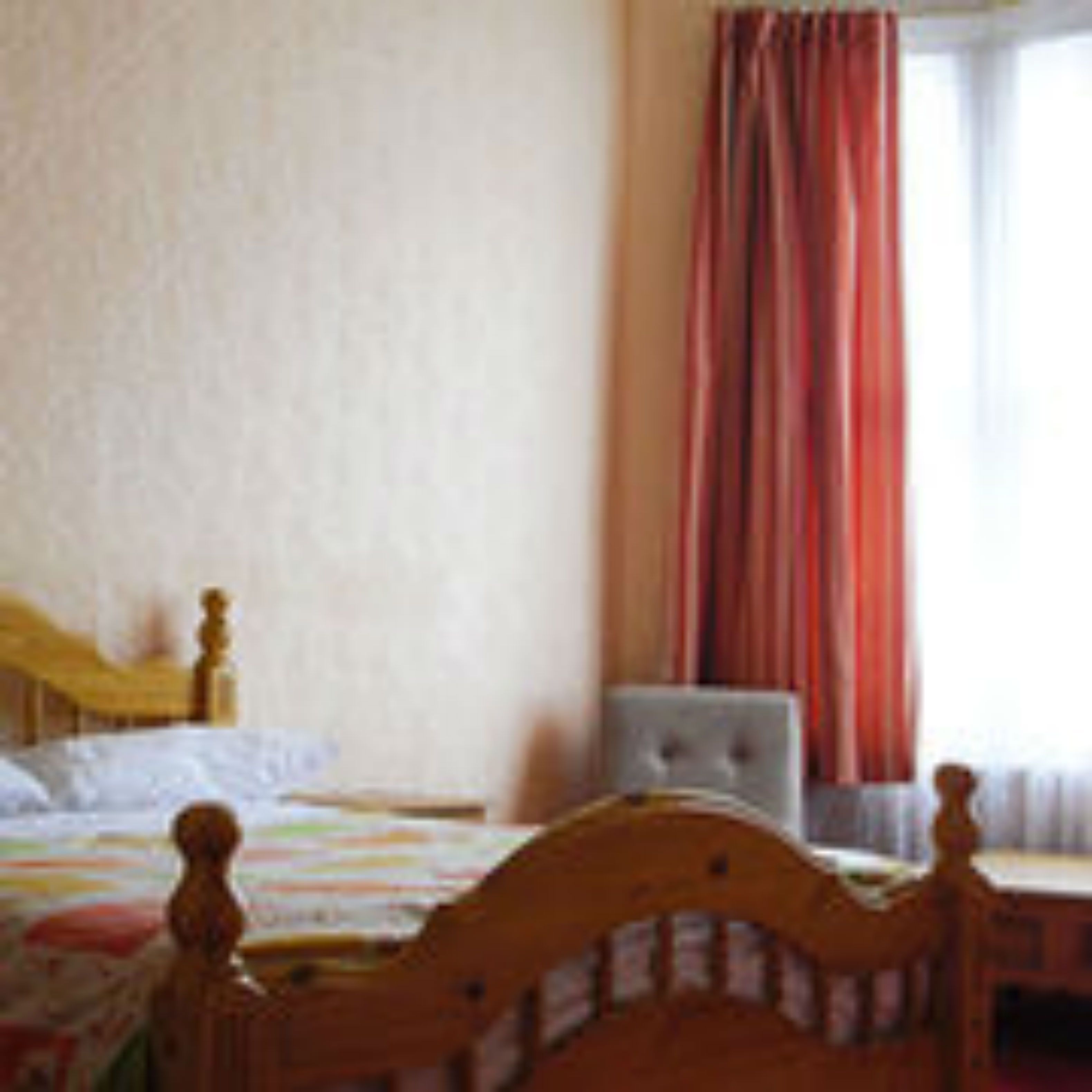 Een slaapkamer met een houten bed, een nachtkastje en een raam met gordijnen.