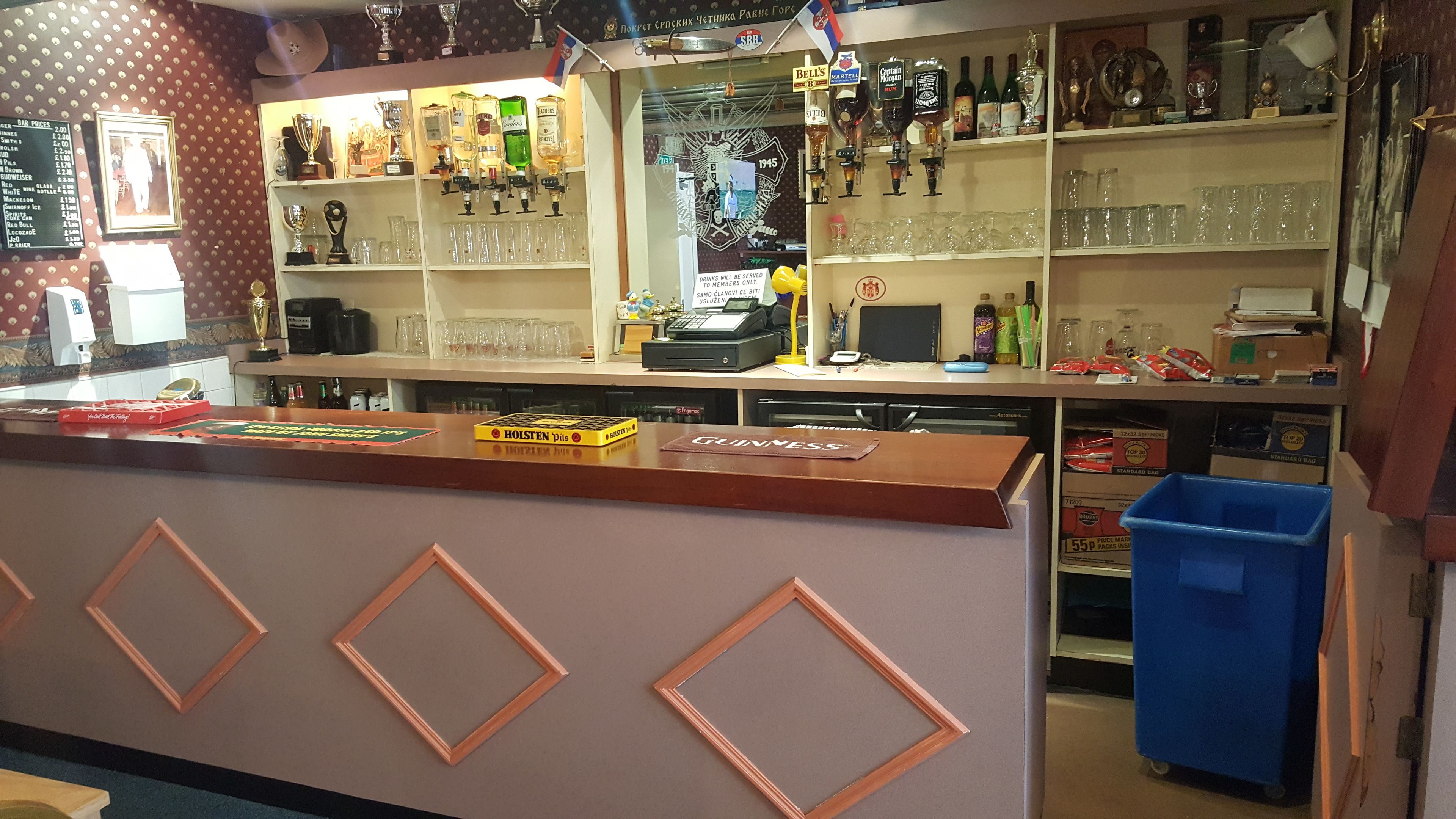 A bar area with shelves of liquor bottles, glasses, and a counter with a sign reading "GUINNESS".