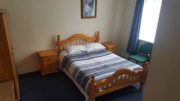 A neatly made bed with a wooden headboard, two bedside tables, a chair, and a painting on the wall.