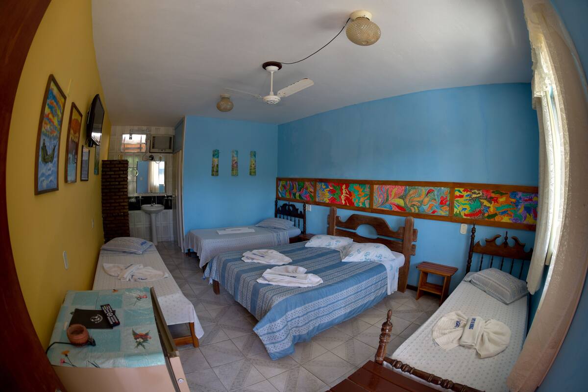 A room with two beds, a ceiling fan, a small table with a remote control, and a wall with colorful artwork.