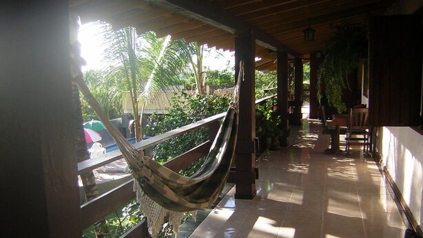 A hammock under a wooden pergola, a tiled floor, and a view of greenery outside. - Pousada Recanto de Minas (Porto Seguro)