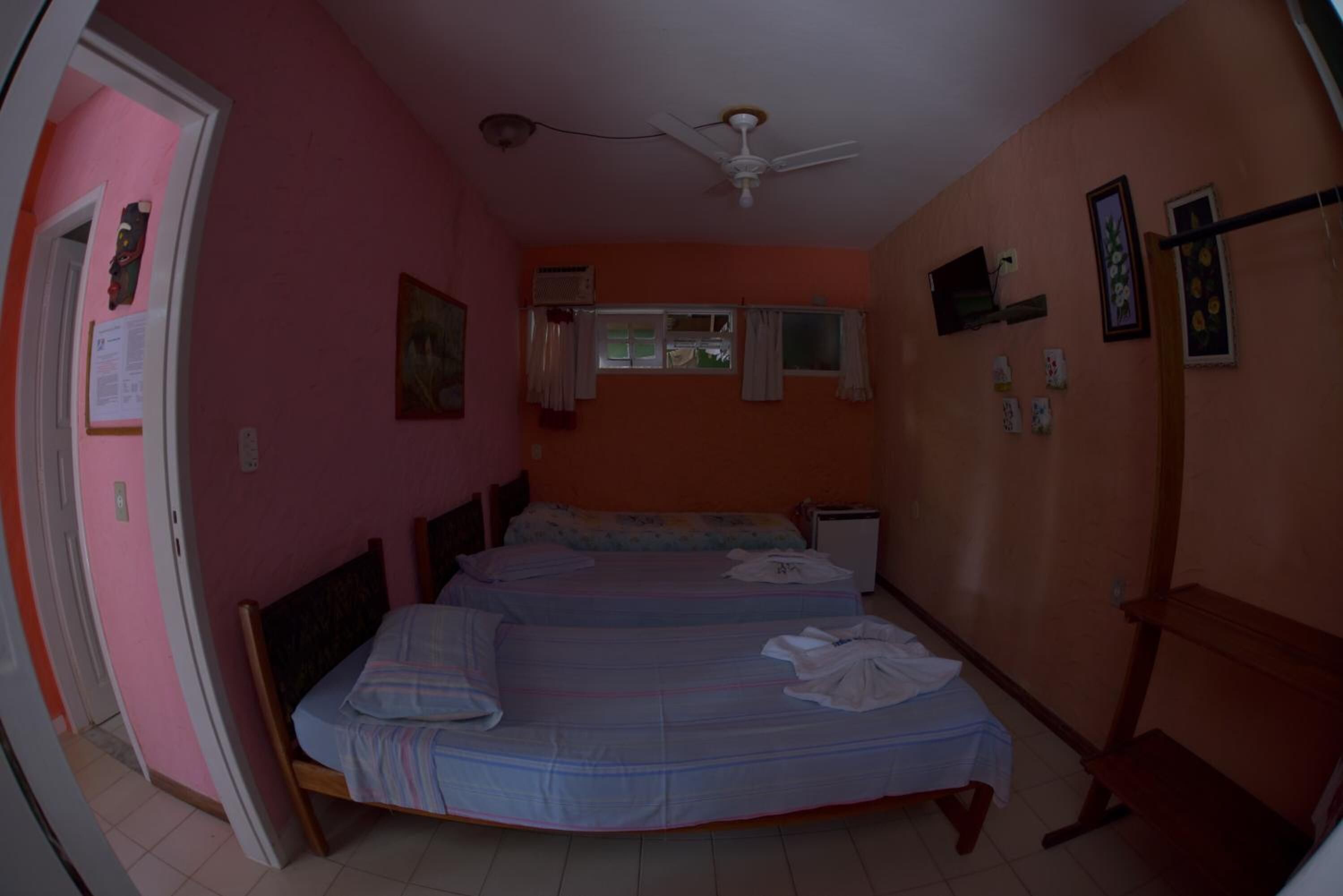 A room with two beds, a ceiling fan, a window with curtains, and a door.