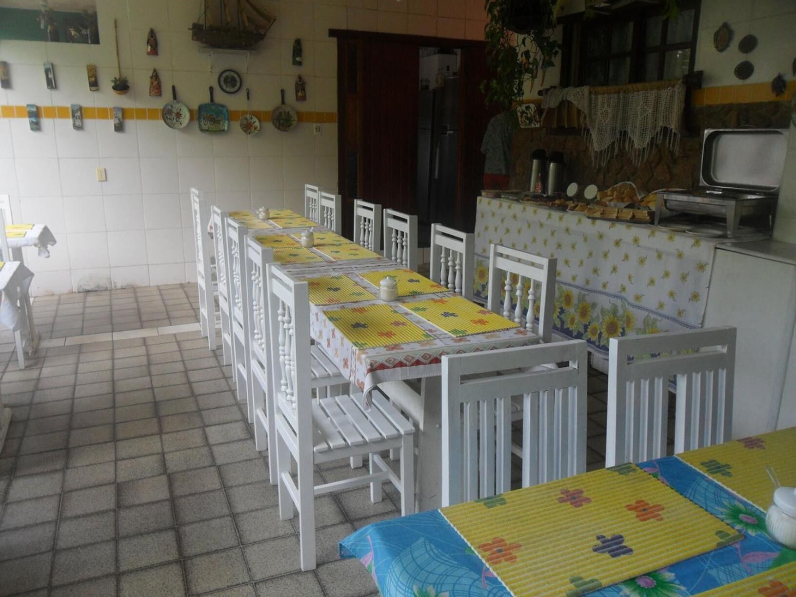 Uma sala de jantar com uma mesa comprida posta para várias pessoas, rodeada por cadeiras brancas.