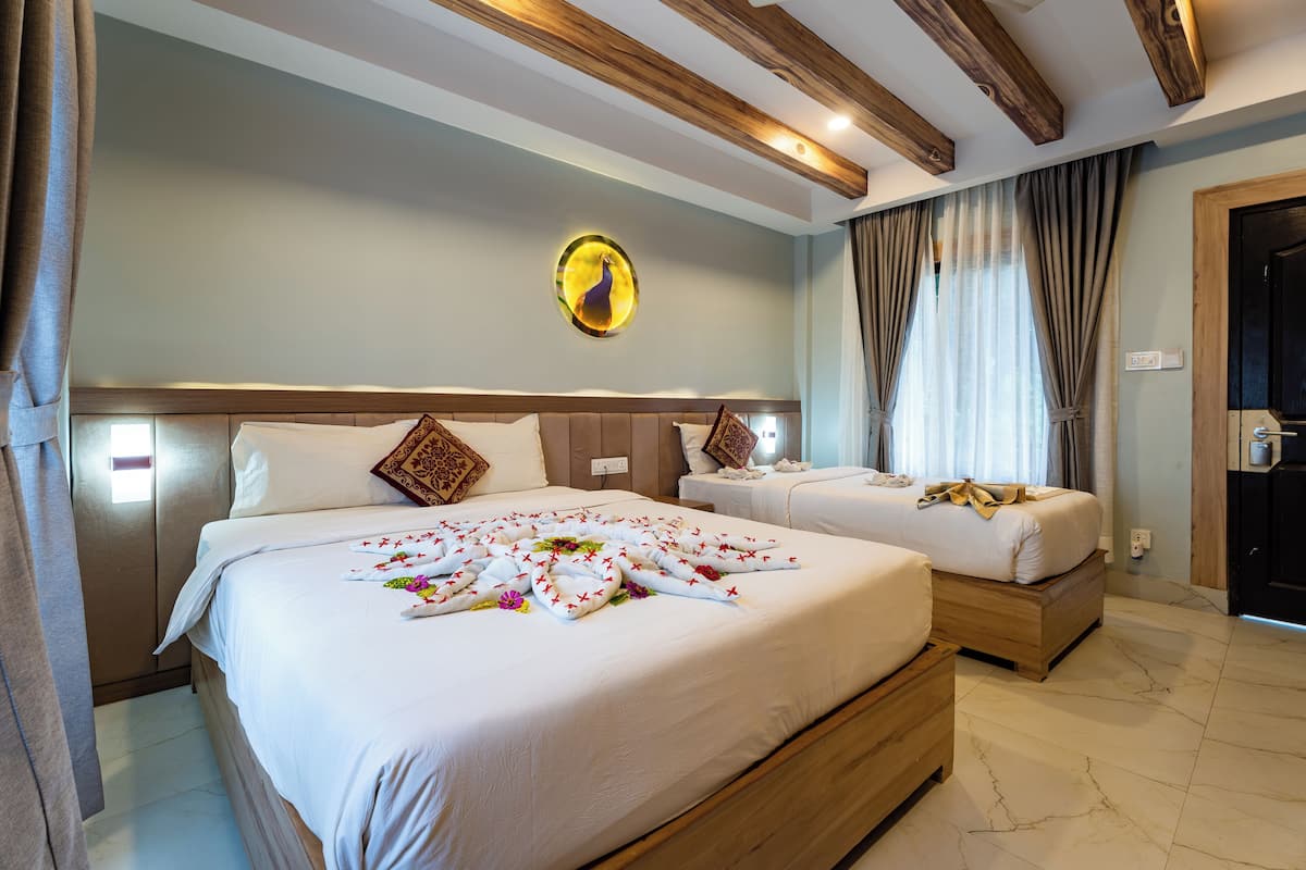 Ein Hotelzimmer mit einem großen Bett, einem kleineren Bett, Holz-Kopfteilen, einer Wandleuchte und einer Tür mit Griff.