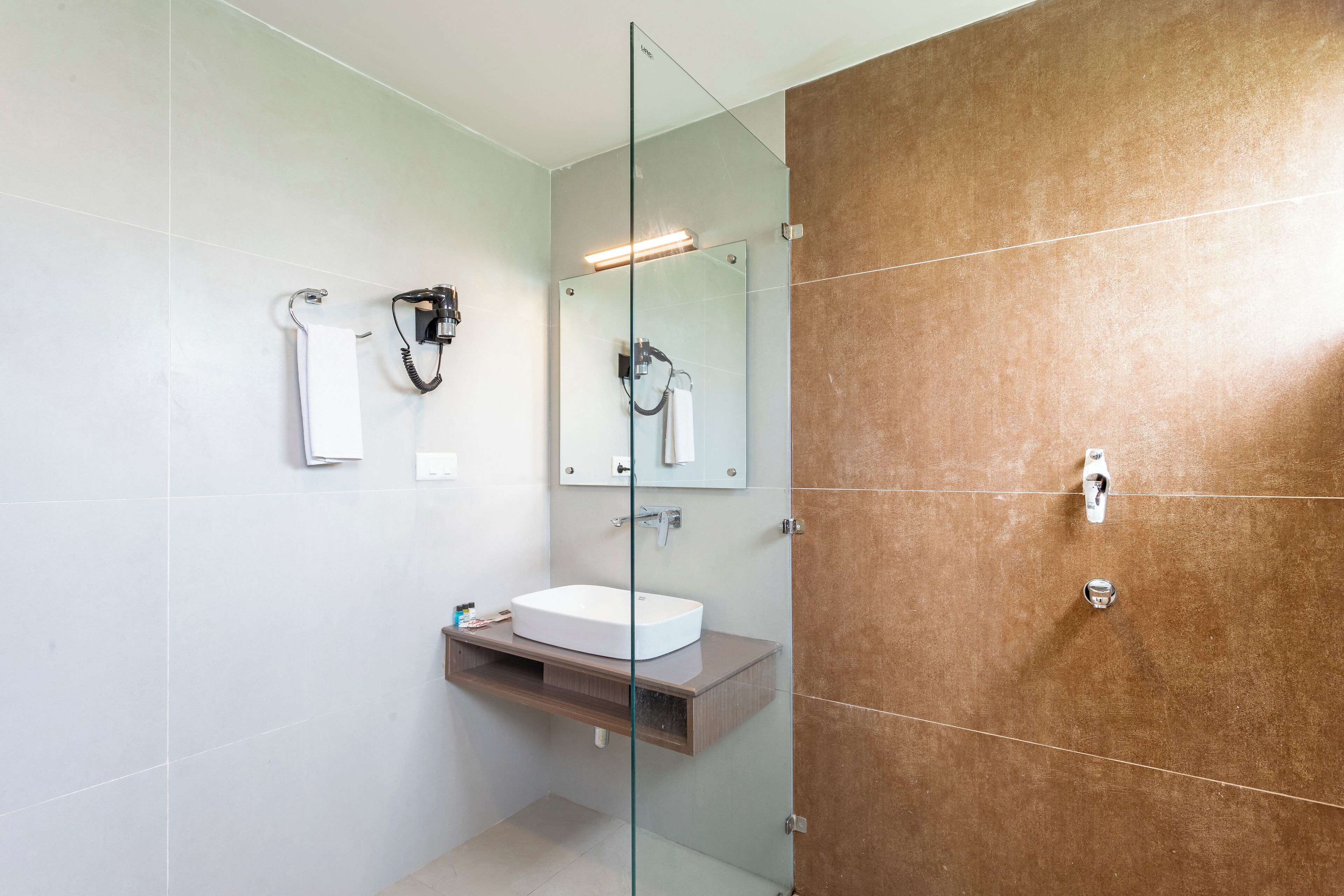 Un baño moderno con cabina de ducha de vidrio, lavabo blanco y pared revestida de baldosas marrones.