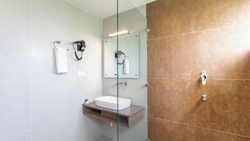 Un baño moderno con cabina de ducha de vidrio, lavabo blanco y pared revestida de baldosas marrones.
