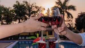 A dining table with plates of food, glasses of red wine, and a poolside view at sunset. - Hotel Seven Limited (Sauraha)