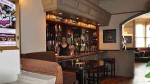 A bar area with a bar counter, stools, and a seating area with a sofa. - The Locomotion Hotel (Stockton-on-Tees)