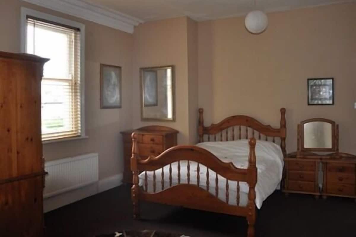 A bedroom with a wooden bed, a dresser, and a window with blinds.