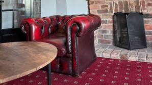A cozy room with a leather sofa, a round wooden table, a brick fireplace, and a wall clock. - The Swan Hotel (Worcester)