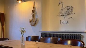 A wooden dining table with chairs, a vase with flowers, and a wall with a swan illustration and text.