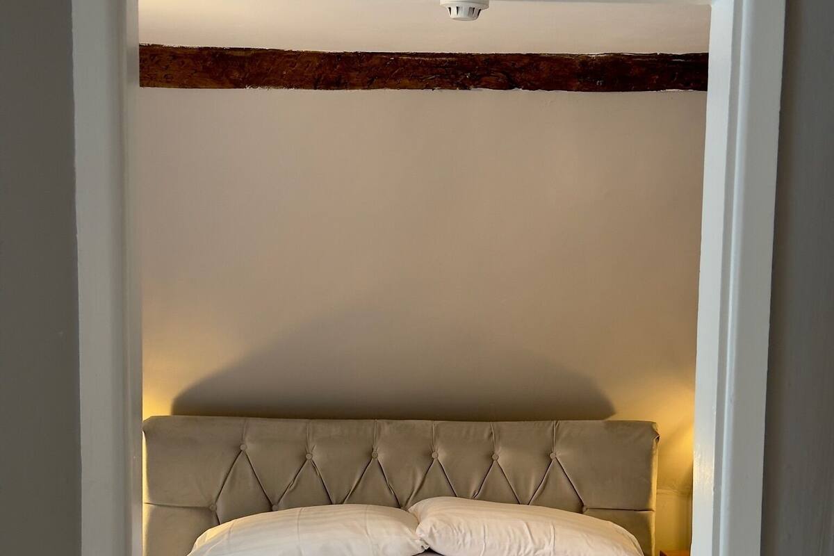 Cama bem arrumada com cabeceira estofada, roupa de cama listrada em branco e dois travesseiros.