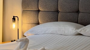 A neatly made bed with a tufted headboard, a bedside lamp, and a rolled towel on the bed. - The Swan Hotel (Worcester)
