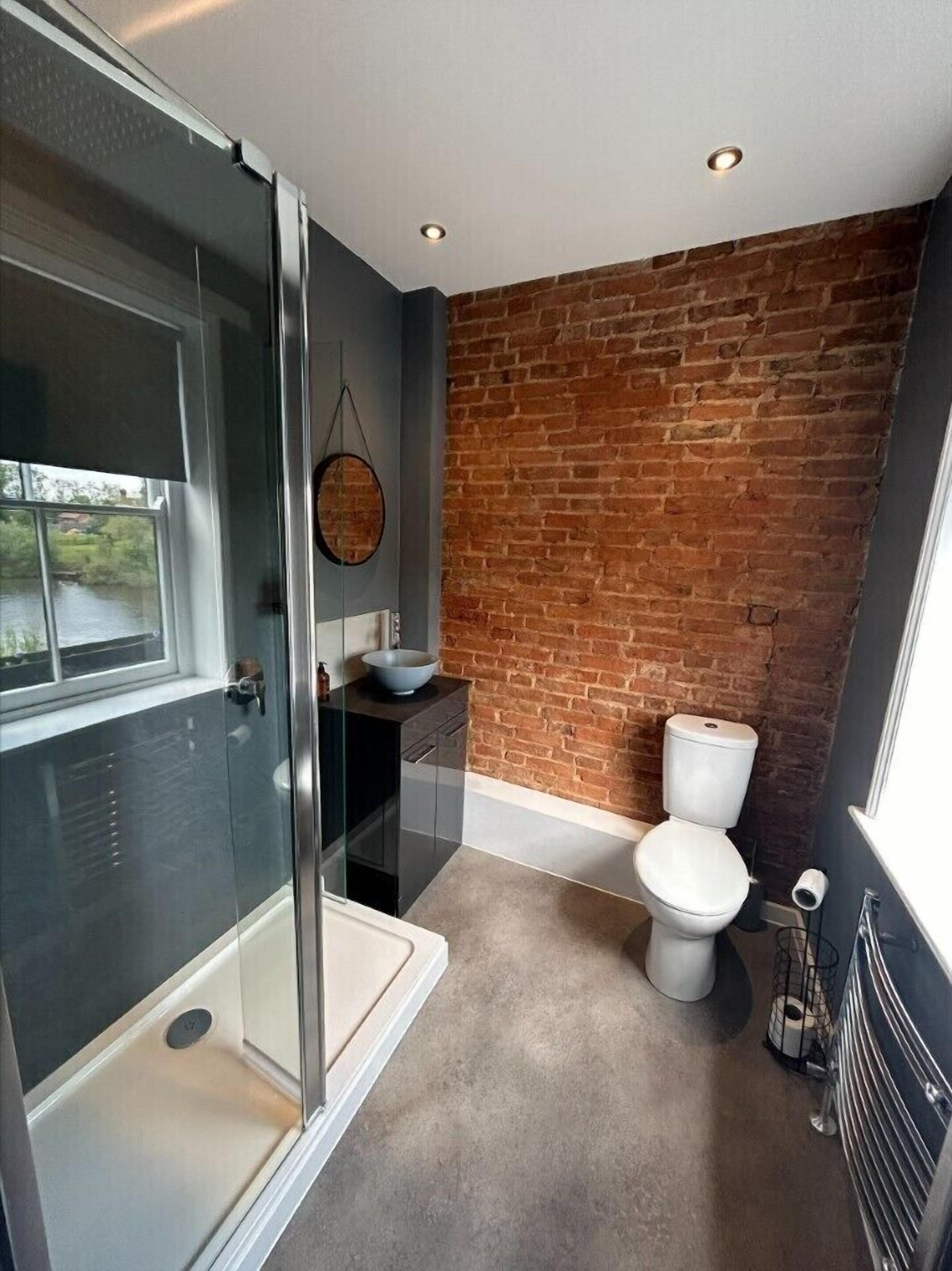 A modern bathroom with a glass shower enclosure, a white toilet, and a brick accent wall.