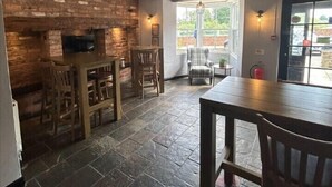 A rustic interior with exposed wooden beams, a brick wall, a stone floor, and a seating area with wooden tables and chairs. - The Swan Hotel (Worcester)