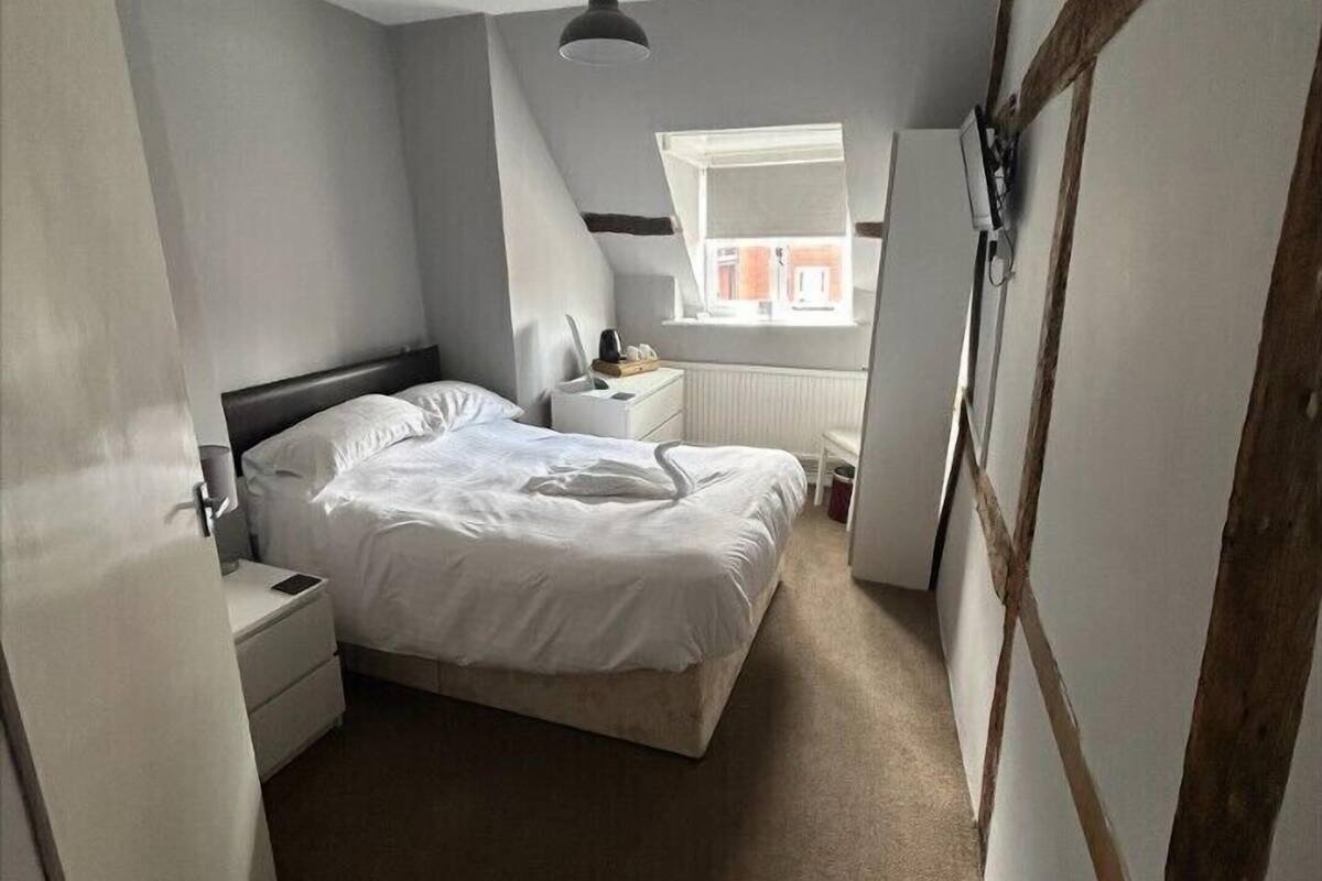 Quarto com cama, mesa de cabeceira, abajur e janela com vista para o exterior.