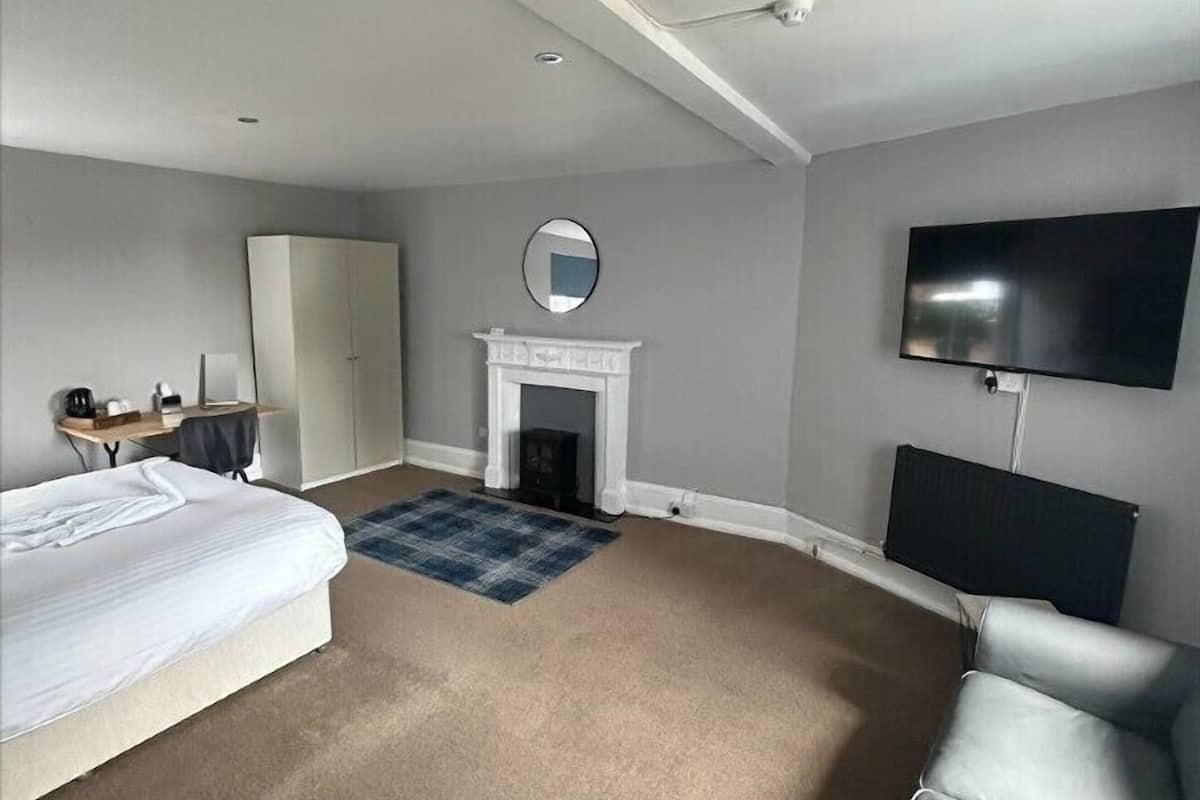Quarto de hotel com cama, escrivaninha, poltrona, lareira, televisão e sofá.