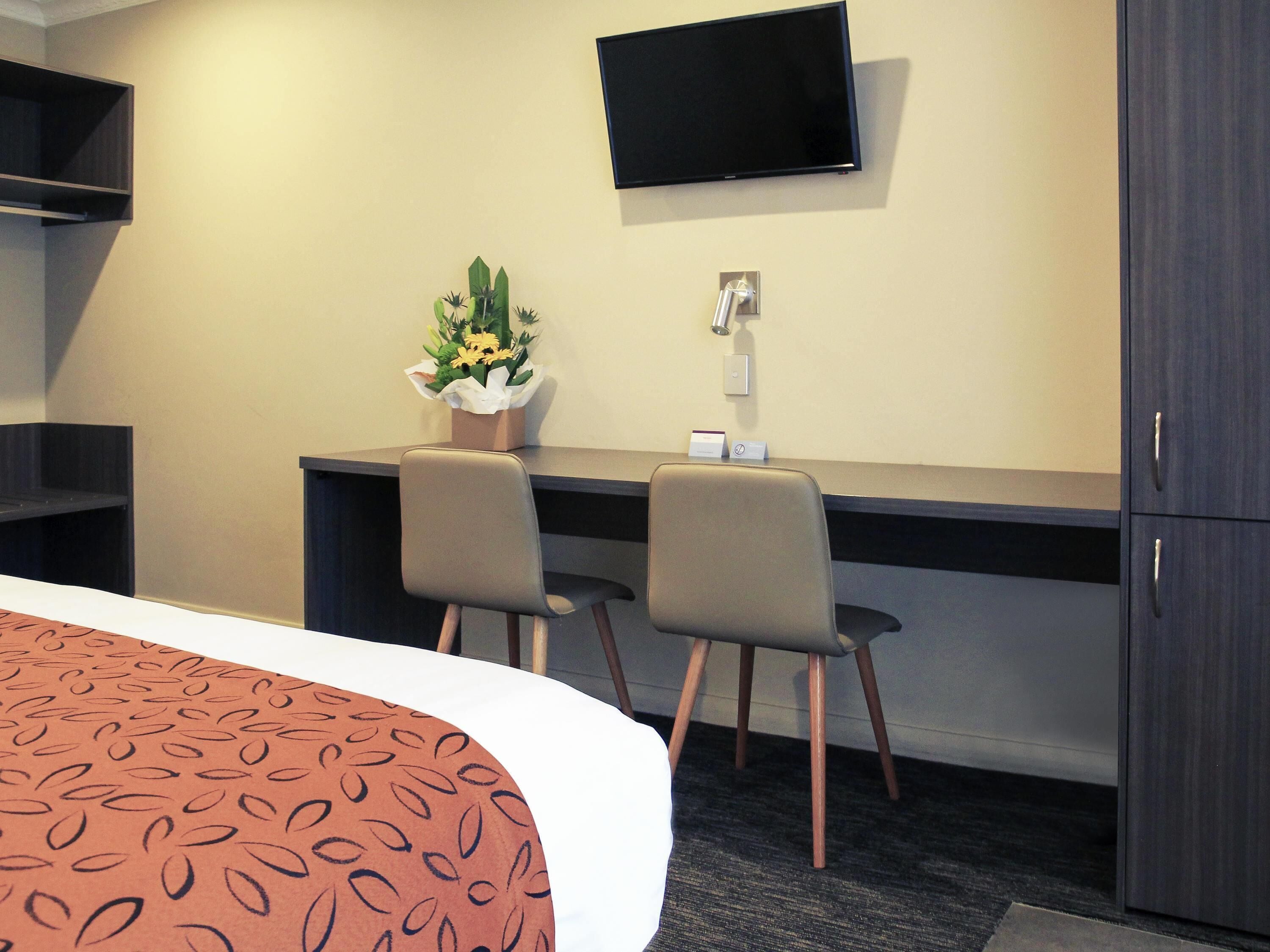 Habitación de hotel con cama, escritorio con dos sillas, televisor de pantalla plana, arreglo floral y armario.