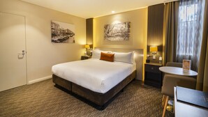 A hotel room with a large bed, two bedside tables with lamps, a small table, and a chair. - Mercure Orange (Orange)