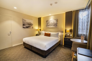 Habitación de hotel con una cama grande, dos mesitas de noche con lámparas, una pequeña mesa y una silla.