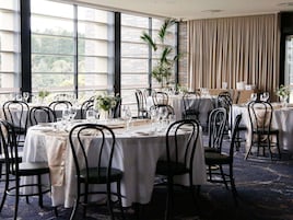 A dining area with round tables, black chairs, and white tablecloths.