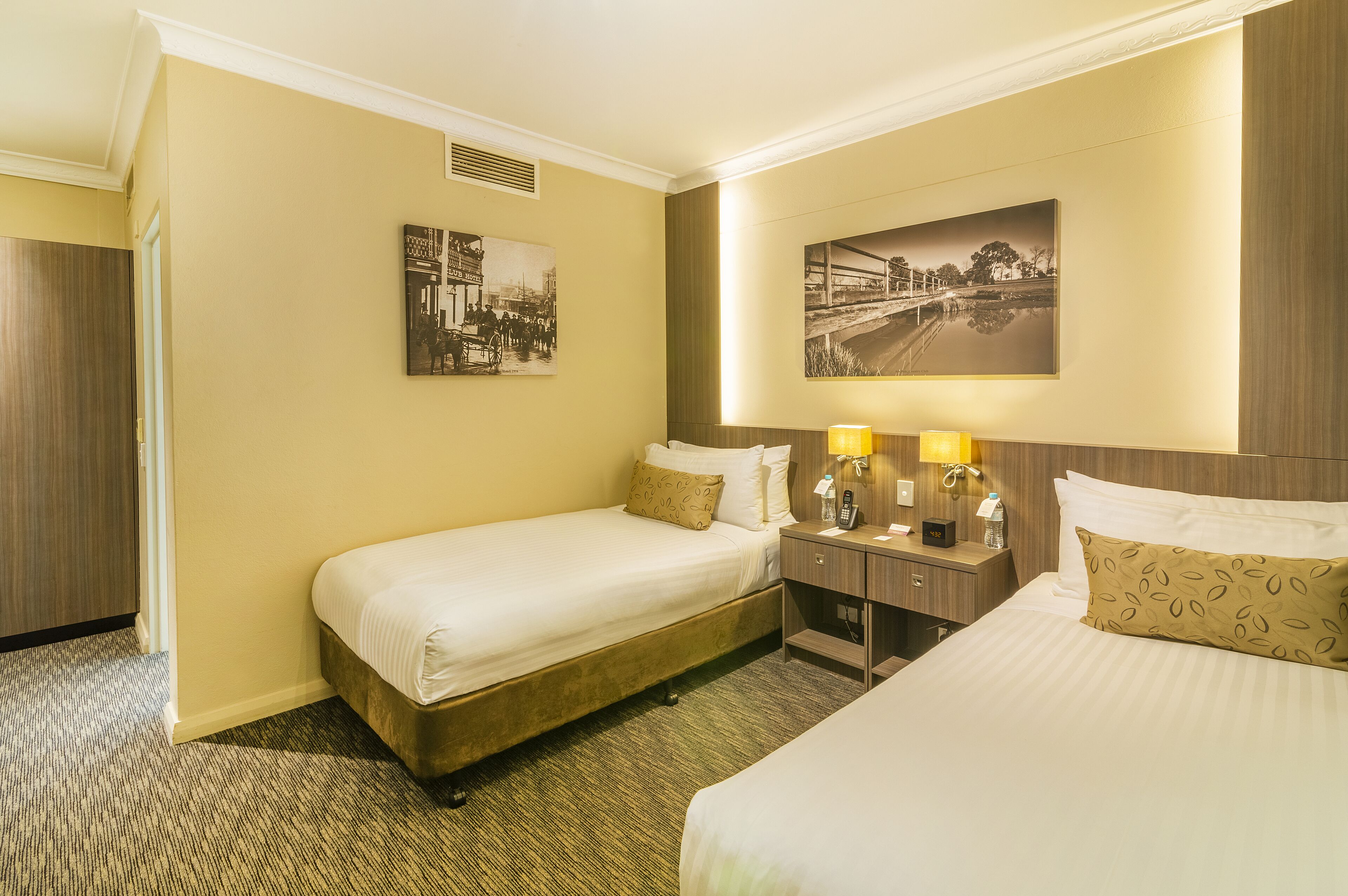 A hotel room with two beds, a nightstand with lamps, a wall-mounted picture, and a door.