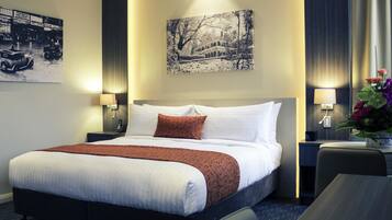 A hotel room with a large bed, two bedside tables with lamps, a wall-mounted painting, and a small table with flowers.