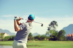 Una persona con camisa gris y gorra azul balanceando un palo de golf.