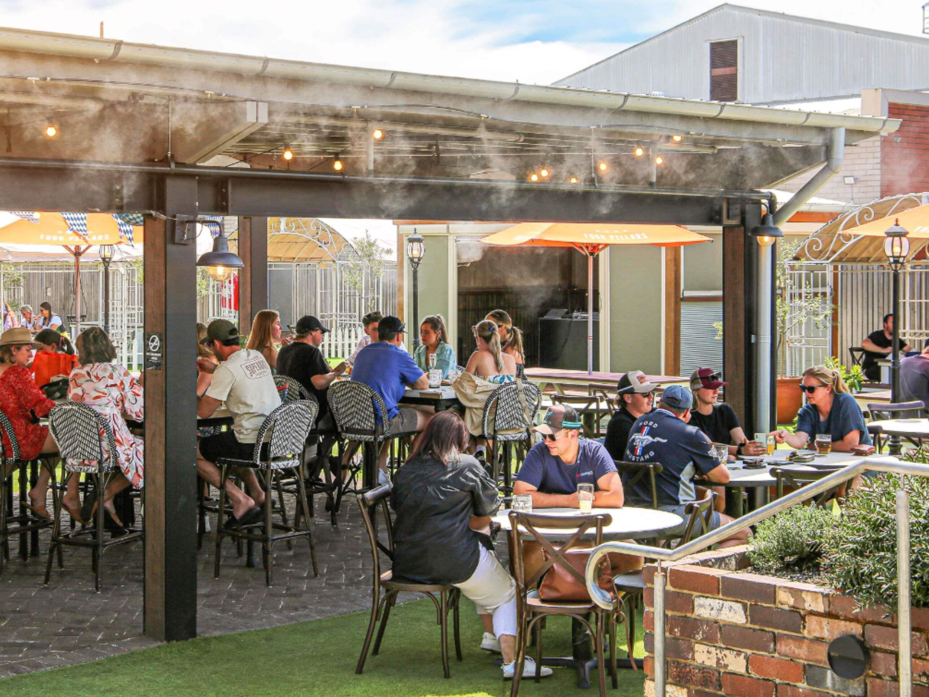 Une terrasse extérieure avec des tables et des chaises, un mur en briques et un espace abrité avec des parasols.