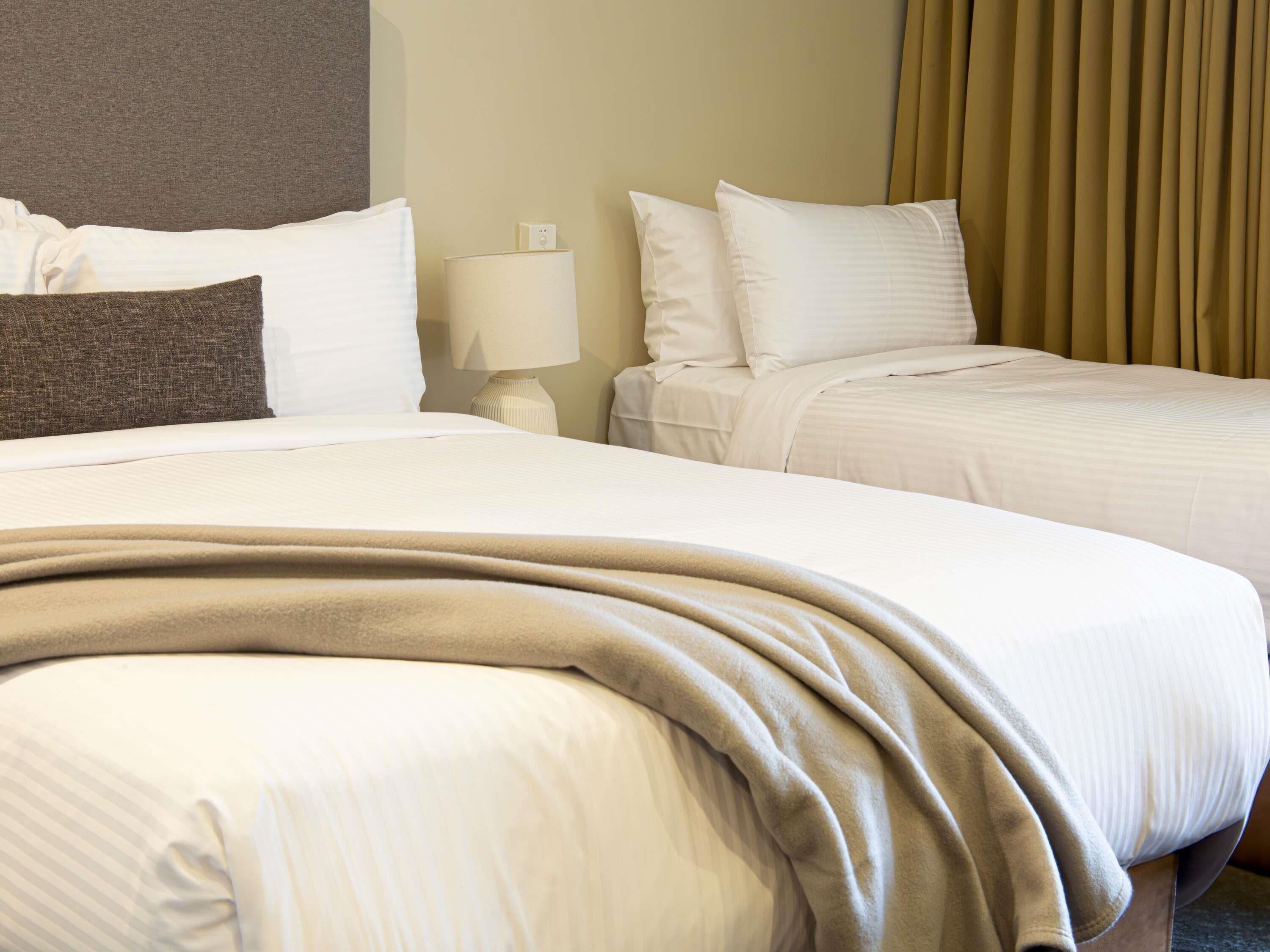 A hotel room with two beds, a lamp, and a curtain.