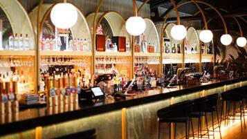 A bar with multiple levels of shelves stocked with bottles, a cash register, and bar stools.