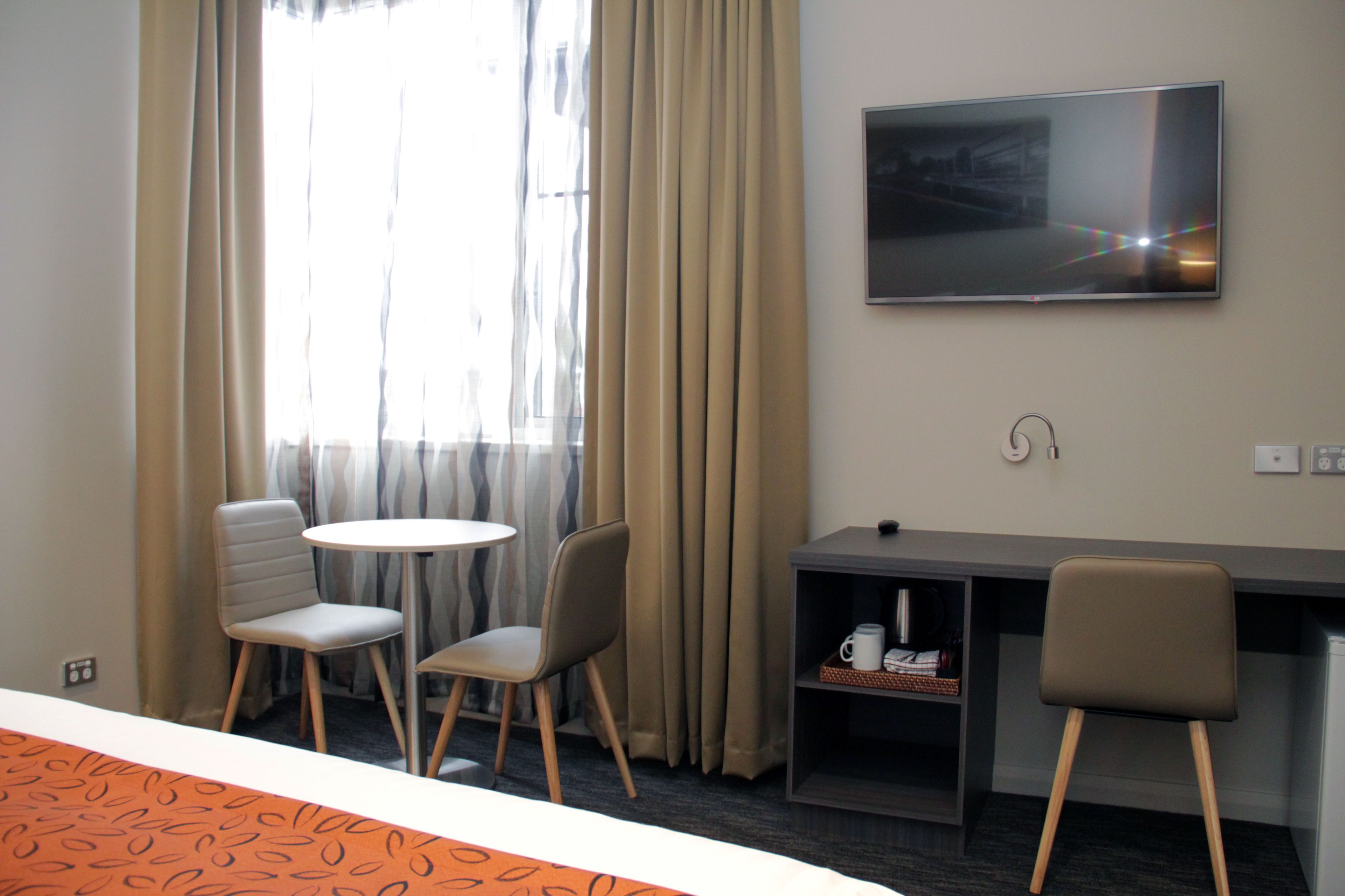 Habitación de hotel con cama, escritorio con silla, televisor y ventana con cortinas.