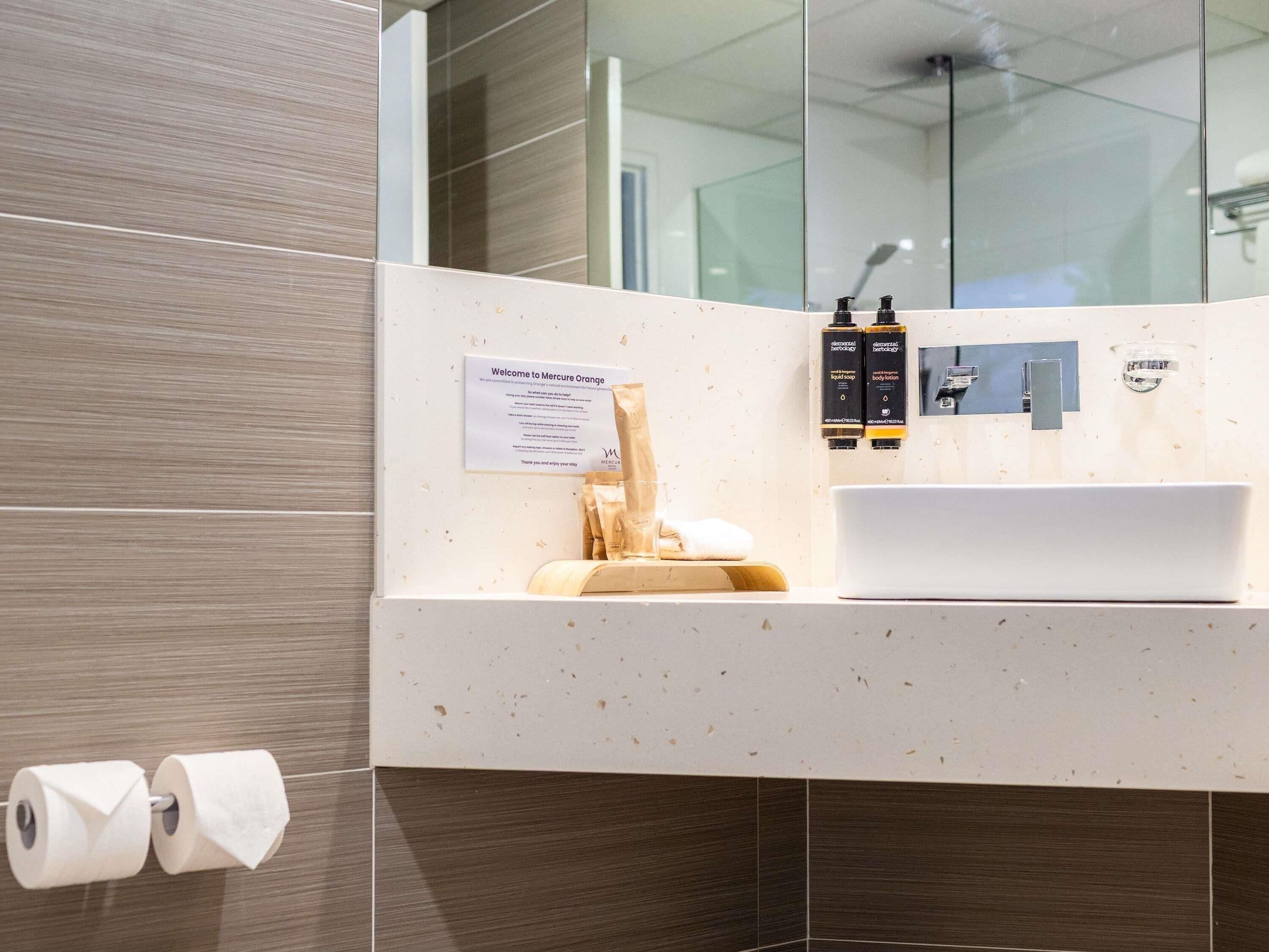 A modern bathroom with a white sink, two toiletries, a towel, and a welcome sign.