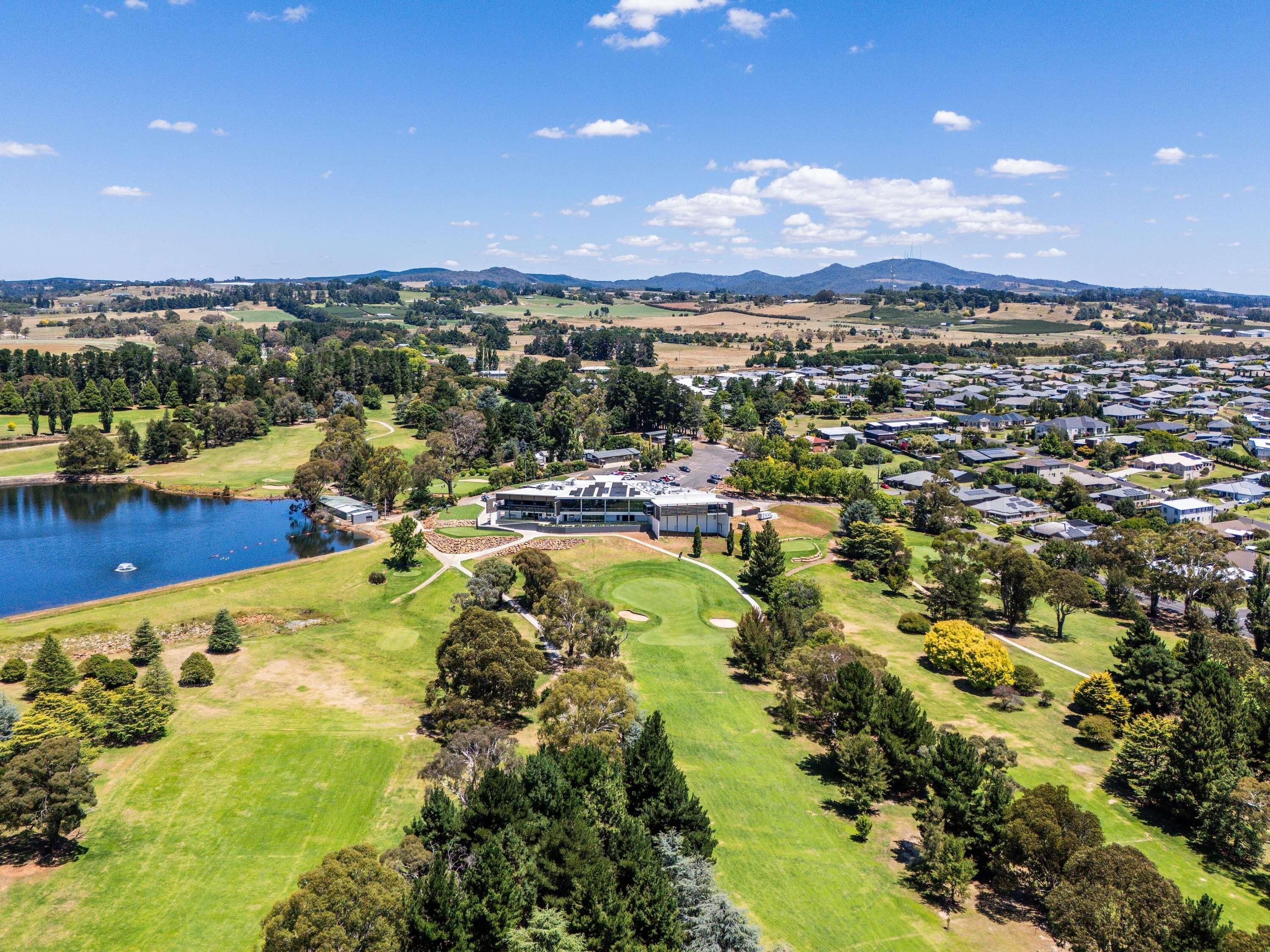 Vista aérea de una zona residencial con un edificio grande, posiblemente un hotel, rodeado de espacios verdes, un lago y un campo de golf.