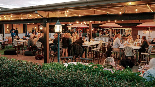 An outdoor dining area with tables and chairs, a covered section with umbrellas, and a white fence in the background. - Mercure Orange (Orange)