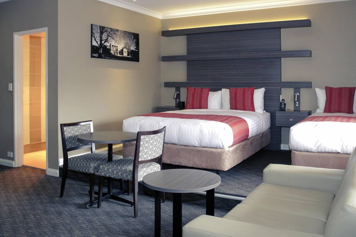 A hotel room with two beds, a dining table, a sofa, and a chair.