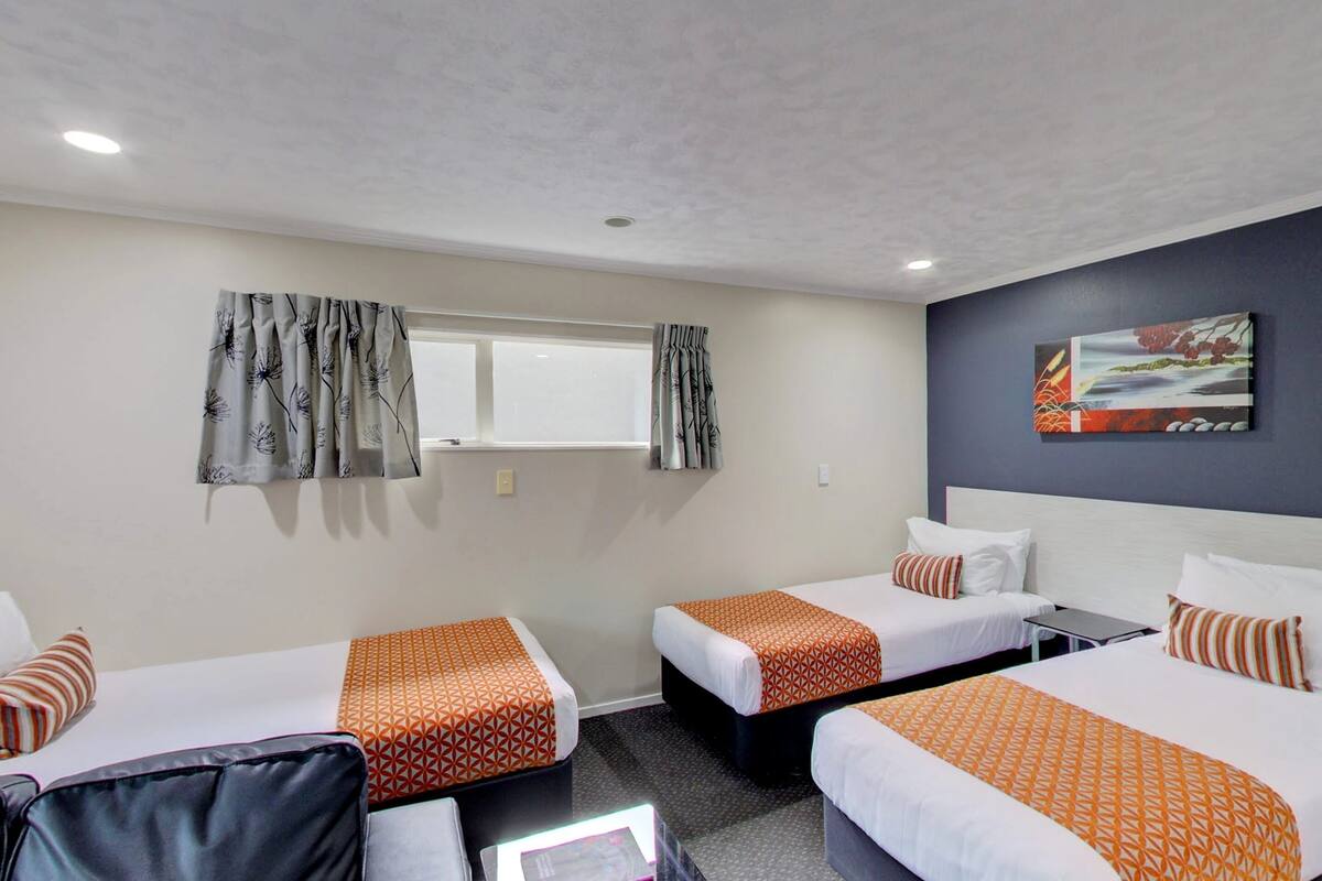 A hotel room with two beds, a desk, and a window with curtains.