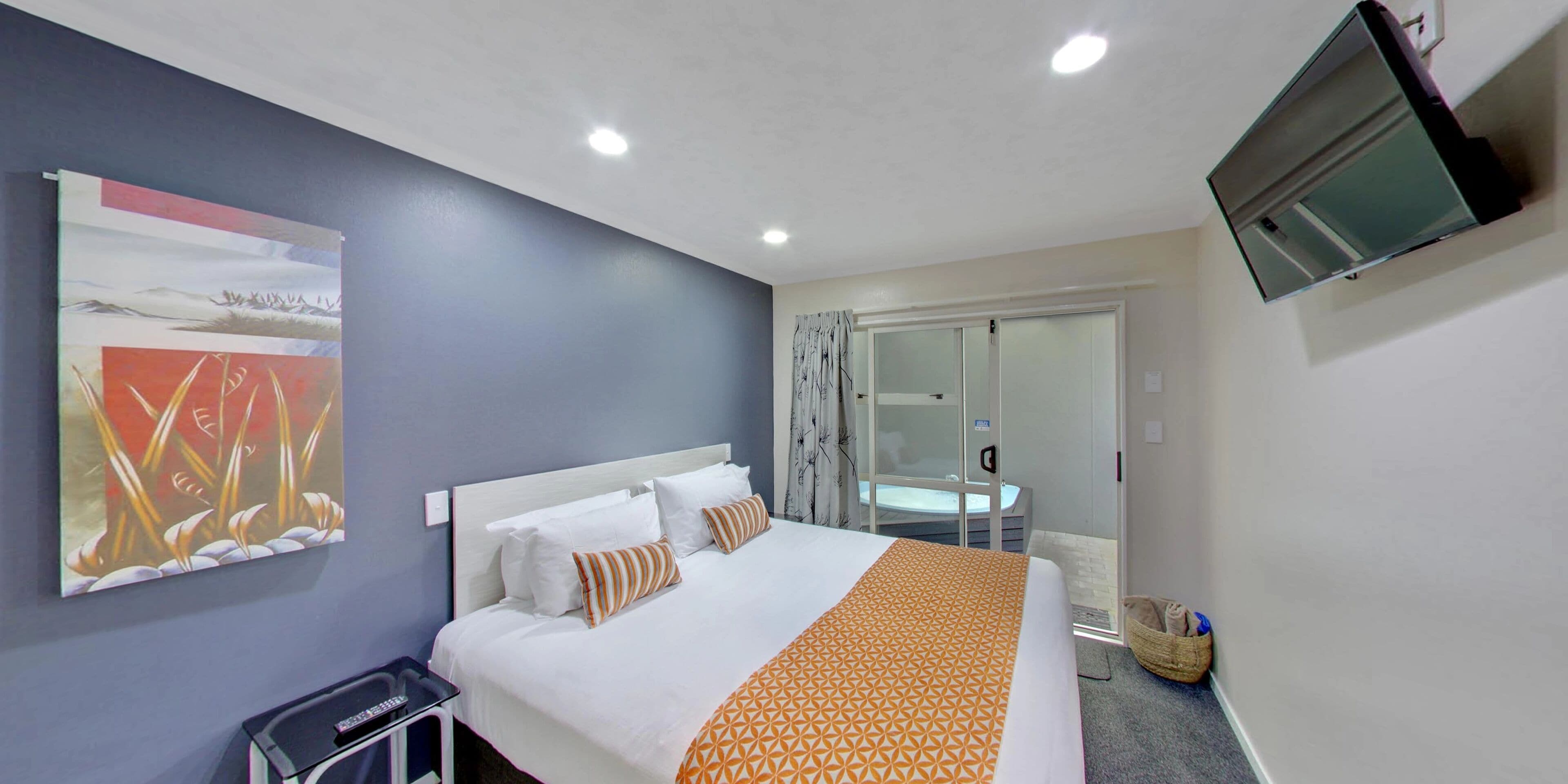 A hotel room with a bed, a TV mounted on the wall, and a window with curtains.