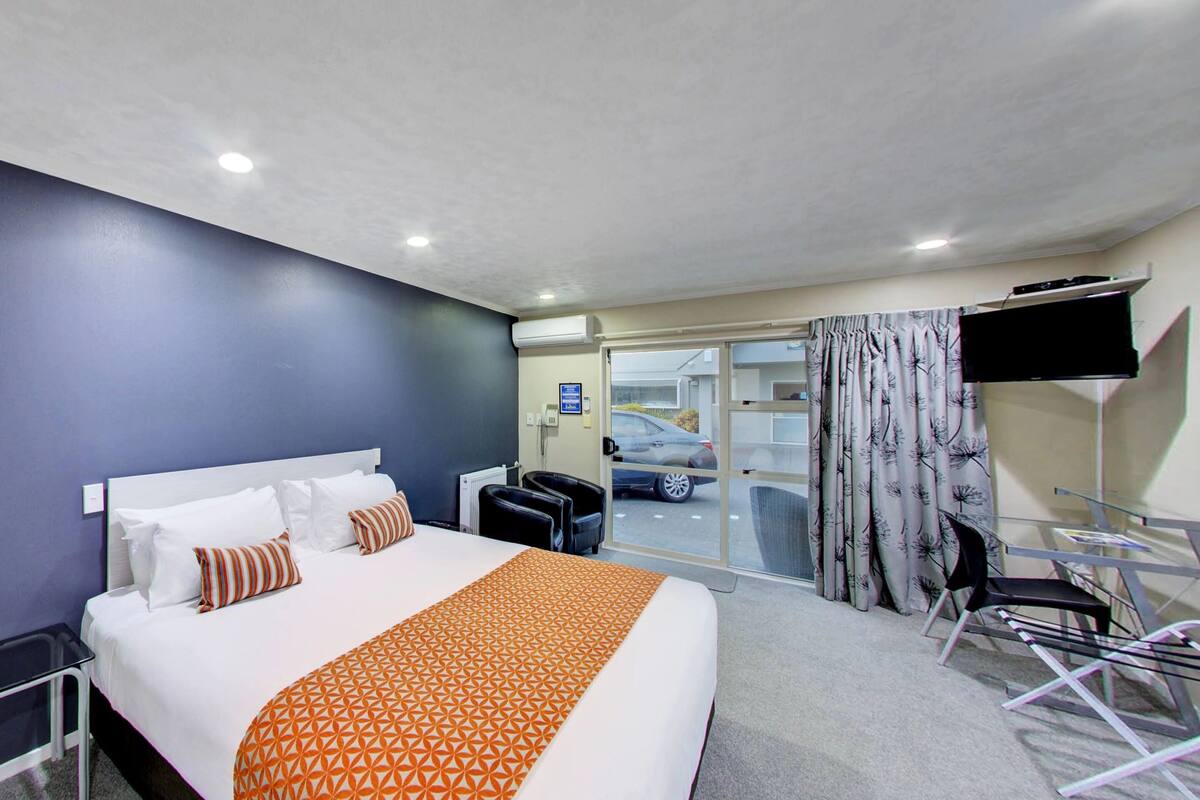 A hotel room with a bed, a desk, a chair, a TV, and a view of the outside.