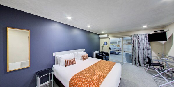 A hotel room with a bed, a desk, a chair, a TV, and a view of the outside. - Capri on Fenton (Rotorua)