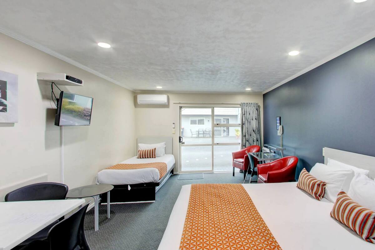 A hotel room with two beds, a desk, a chair, a TV, and a view of the outside.