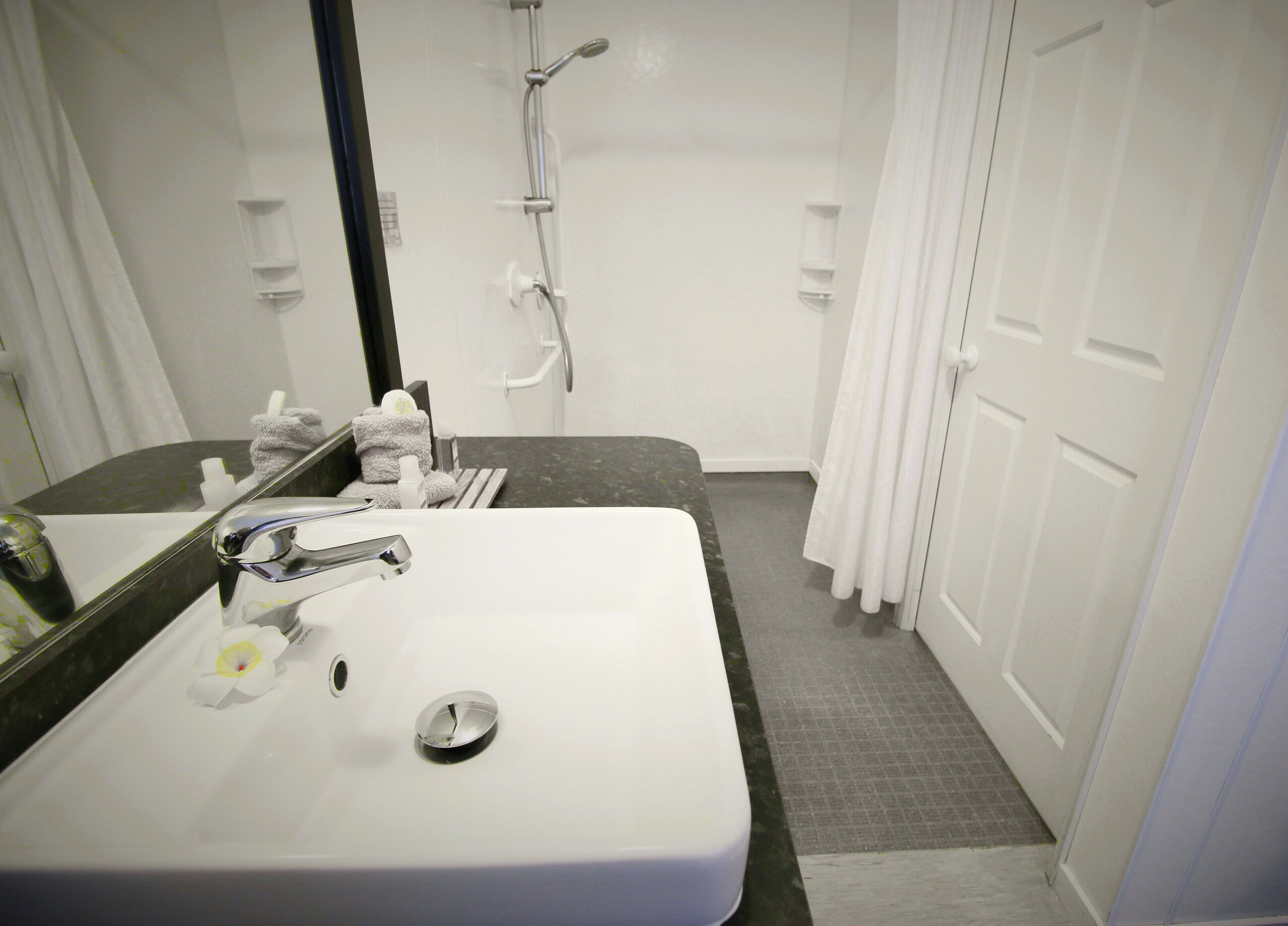A bathroom with a white sink, a mirror, a towel rack, and a shower area.