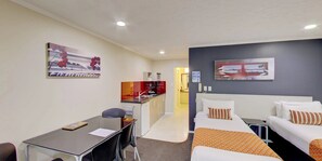 A hotel room with a bed, a desk, and a kitchenette. There is a painting on the wall and a window with a view. - Capri on Fenton (Rotorua)